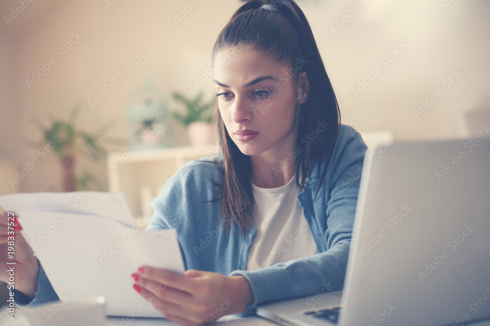 Serious young woman working at home and checking bills. Serious young woman working at home and checking bills.