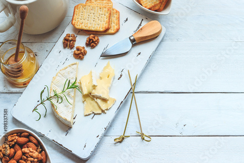 Cheese plate served with crackers, honey and nuts. Camembert on white wood serving board over white texture background. Appetizer theme. Top view with space