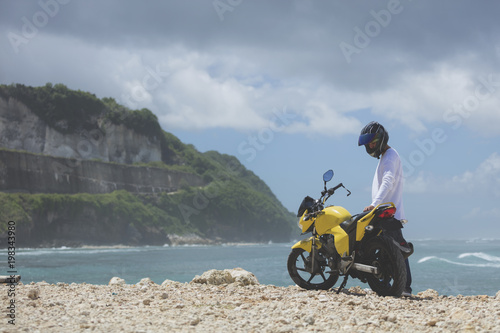 Young handsome man standing with motorcycle on the tropical beach.