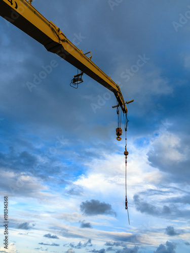 Offshore pedestal crane or lifting machine perform boom up with main and auxiliary hook in blue sky.