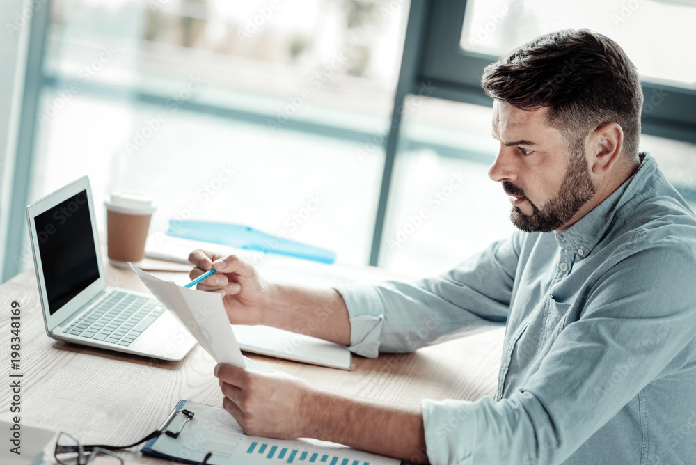 Obraz premium Some problems. Shocked bearded businessman sitting in semi position and leaning elbows on workplace while looking at result