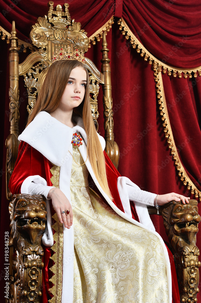 Beautiful teen girl with crown sitting in vintage armchair
