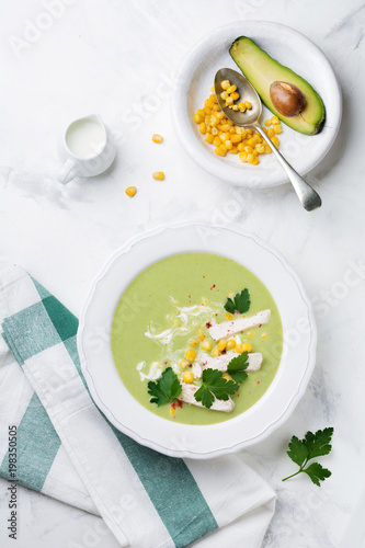 Homemade green soup puree from broccoli, avocado, chicken and corn with cream in rustic ceramic plate on white concrete background. Selective focus. Top view.