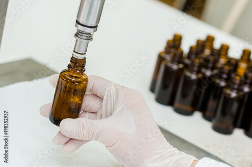 Close up of female lab worker hand with gloves filling the bottle with syrup