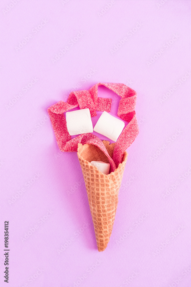 Creative flat lay on purple background. Waffle cone, marshmallows, and red marmalade stripes. Copy space for text, minimalism