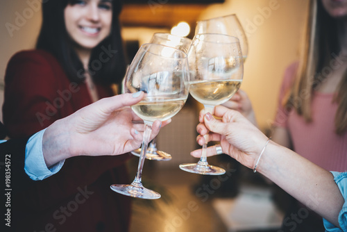 Happy friends cheering with glasses of white wine, celebrating party, girlfriends making a toast at birthday party in modern loft, enjoying and anniversary concept, focus on a hands