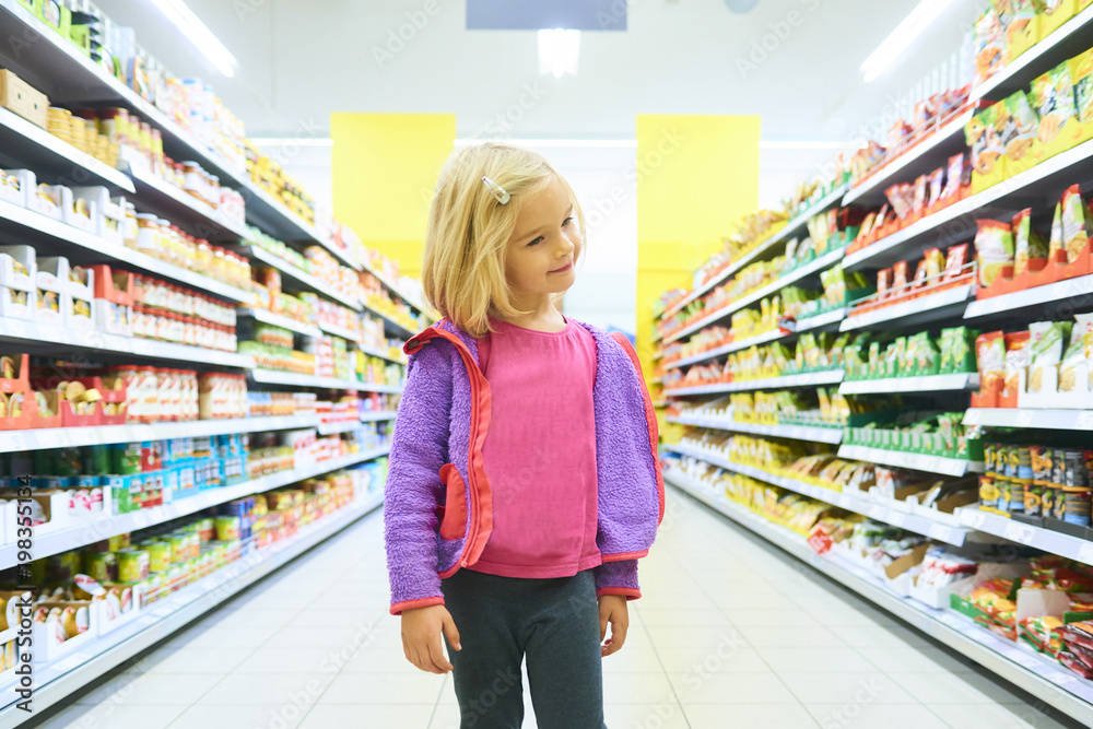 Little Child Blond Girl Shopping in the supermarket, pushing trolley, looking for sweets