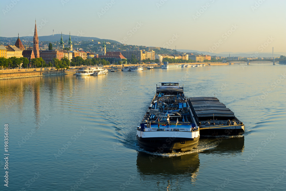 Fototapeta premium cargo ship carrying a barge side by side along still Danube river in Budapest