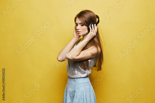Sexy and beautiful model girl in headphones listening music over yellow background