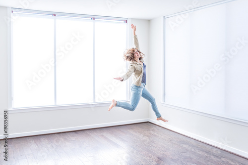 Fotografi One young happy woman jumping up in empty modern new room with hardwood floors a