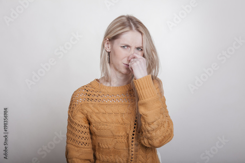 blonde frau hält sich die nase zu weil sie ekelhaften gestank wahrnimmt. sie macht ein angestrengtes gesicht.