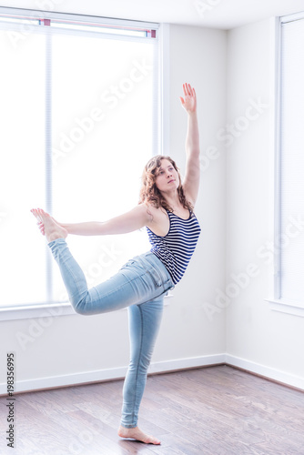 Fototapeta Naklejka Na Ścianę i Meble -  Young happy woman stretching dancing in empty modern new room with hardwood floors and large sunny windows in apartment