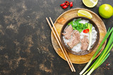 Traditional Vietnamese pho soup with rice noodles and beef in a bowl on a wooden tray. Dark background, top view, copy space.