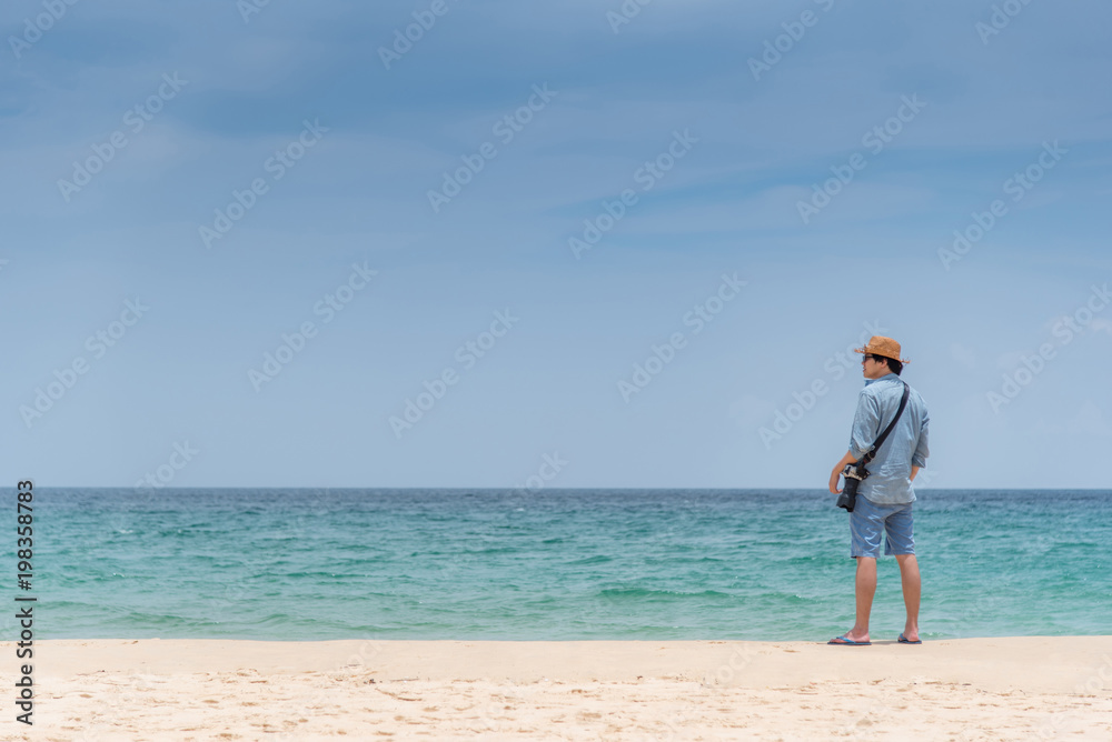 Young Asian man photographer standing on the beach. sea and sky horizon in background. Travel holiday or vacation in summer season concept Young Asian man photographer standing on the beach. sea and sky horizon in background. Travel holiday or vacation in summer season concept