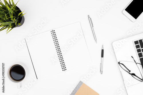 Blank notebook is on top of white office desk table with laptop  coffee cup and office supplies. Top view with copy space  flat lay.
