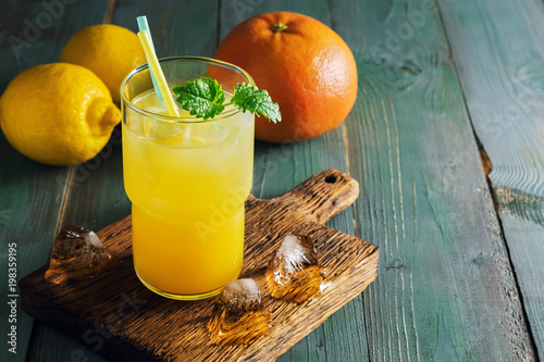 Foto Refreshing lemon orange drink with ice and mint on a rustic blue table with backlighting