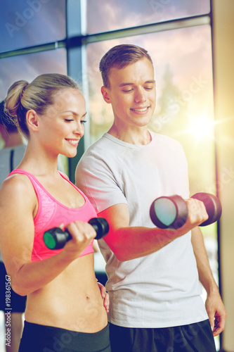 fitness, sport, exercising and diet concept - smiling young woman and personal trainer with dumbbells in gym