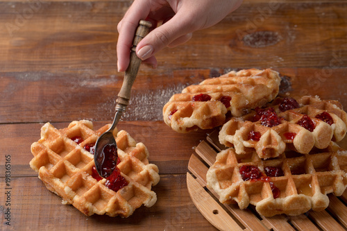 A wooden spoon with strawberry jam and delicious waffles. Traditional breakfast. photo