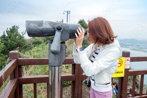 Asian woman looking a big binoculars to see the landscape of park, Jeju Island, Korea