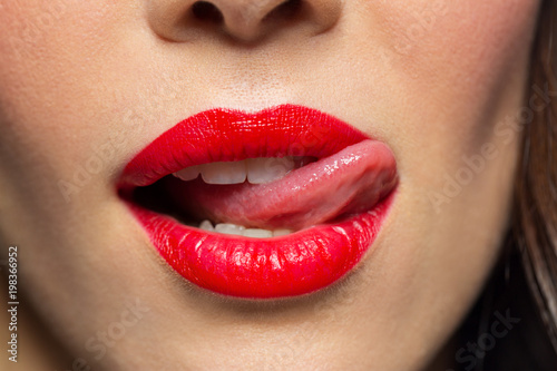 beauty, make up and mouth expression concept - close up of woman face with red lipstick licking her lips