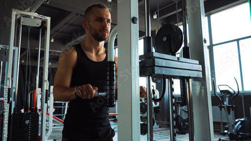 Handsome man doing exercise in the simulator with one hand in fitness gym