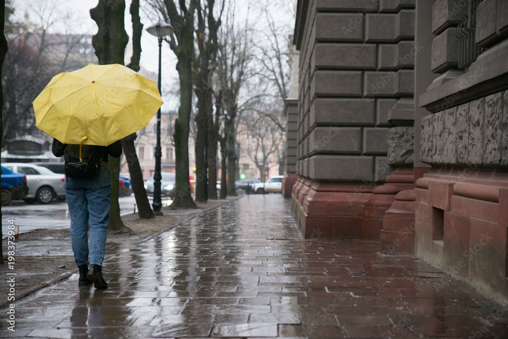 woman walk by old european streets in rainy weather with yellow umbrella. copy space