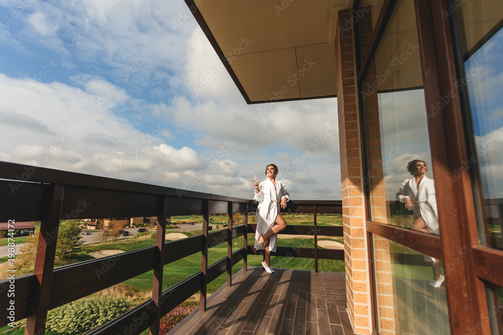 Young happy woman with glass of wine, standing on balcony of apartment and looking at beautiful landscape Young happy woman with glass of wine, standing on balcony of apartment and looking at beautiful landscape