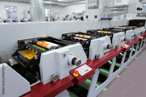 Flexographic printing machine with an ink tray, ceramic anilox roll, doctor blade and a print cylinder with polymer relief plate stuck on it. In-line press machine. Rotary or Flexo printing machine. photo