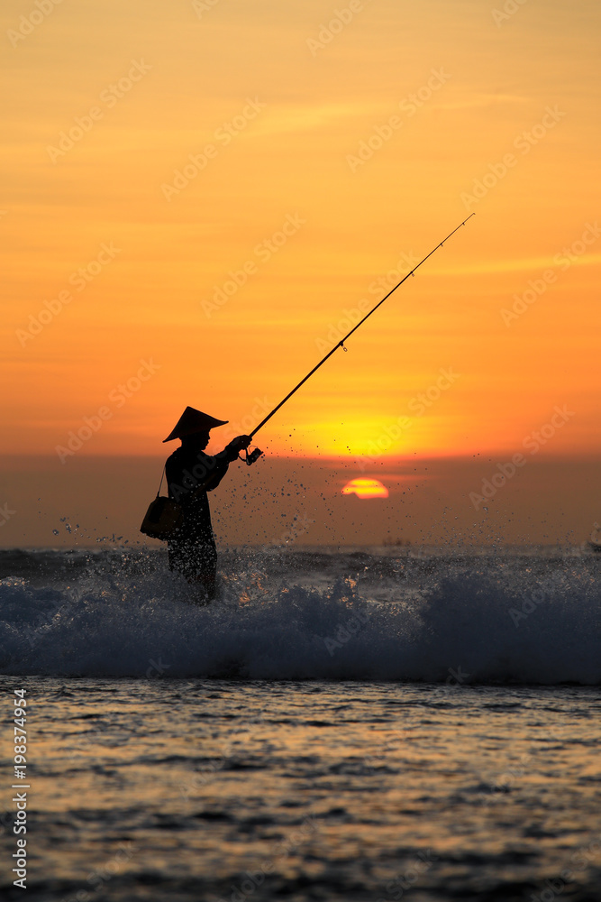 Silhouette of fishermen on the quiet ocean with the rays of sunset at Jimbaran beach, Bali, Indonesia