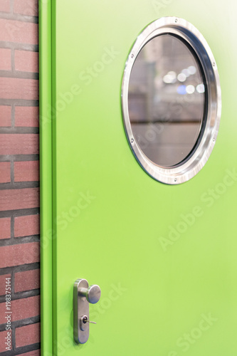 A green door with a round window in a brick wall. photo