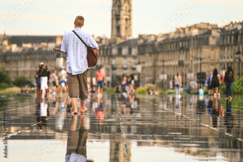 Fototapeta Naklejka Na Ścianę i Meble -  Selective focus on a man holding guitar at Bordeaux water mirror full of people in one of the hotest summer day, having fun in the water