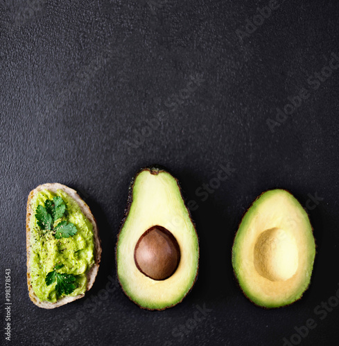 Avocado guacamole on toast bread with spices with Half of avocado on a black background with cop space for text, top view.