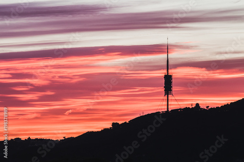 This is a telecommunications tower in Barcelona. It is sunset time and the sky has spectacular colors as purple, orange and red.