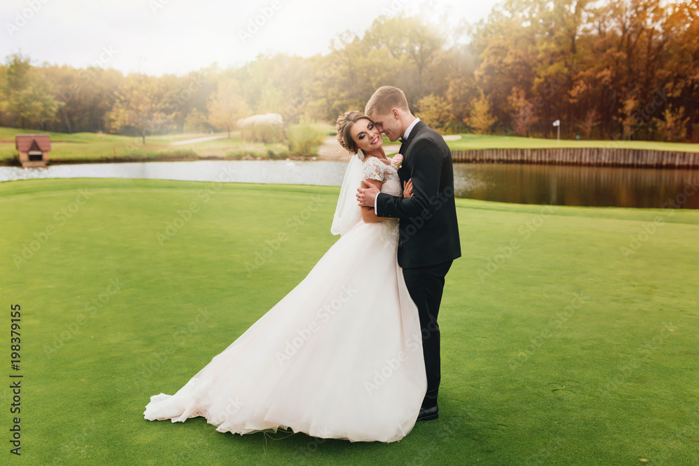 A wedding couple is standing on the green grass near the lake A wedding couple is standing on the green grass near the lake