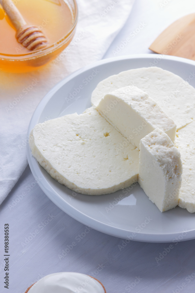 Cheese, honey and sour cream, feta in a white plate, soft cheese on a white background, wooden spoon with sour cream, French breakfast, blue napkin, honey in glassware, art Cheese, honey and sour cream, feta in a white plate, soft cheese on a white background, wooden spoon with sour cream, French breakfast, blue napkin, honey in glassware, art