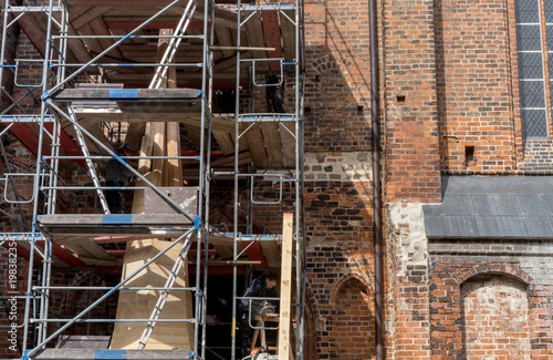scaffolding with church spire / Scaffolding in front of the wall of a gothic brick church with the unfinished church spire