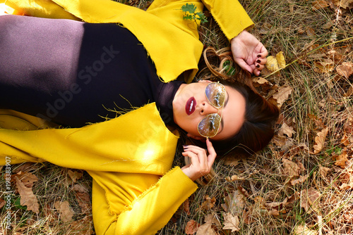 A girl in a black combedress and a yellow coat lies on the grass. photo