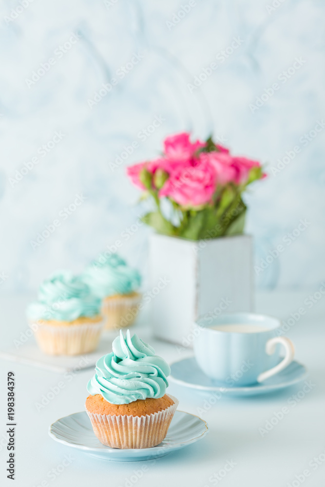 Blue pastel vertical banner with decorated cupcakes, cup of coffe with milk and bouquet of pink roses.
