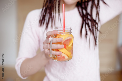 Young pretty woman holding mason jar with lemonade indoors.