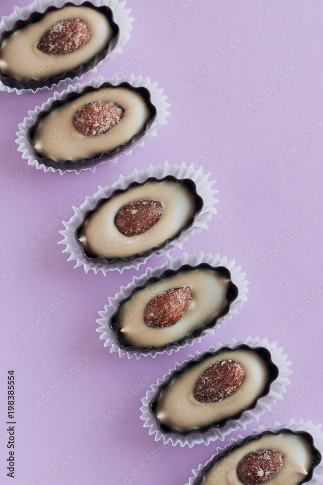 Composition of delicious praline sweets with almonds on purple background