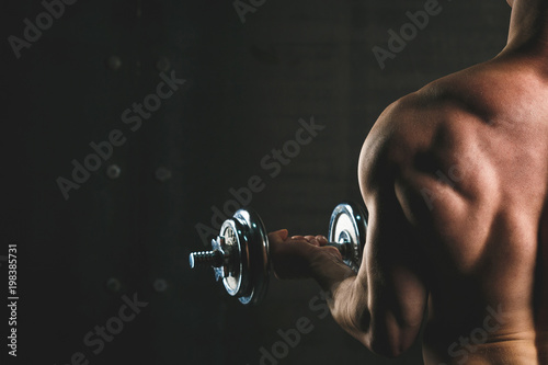Shirtless bodybuilder doing exercises on biceps over grey wall.