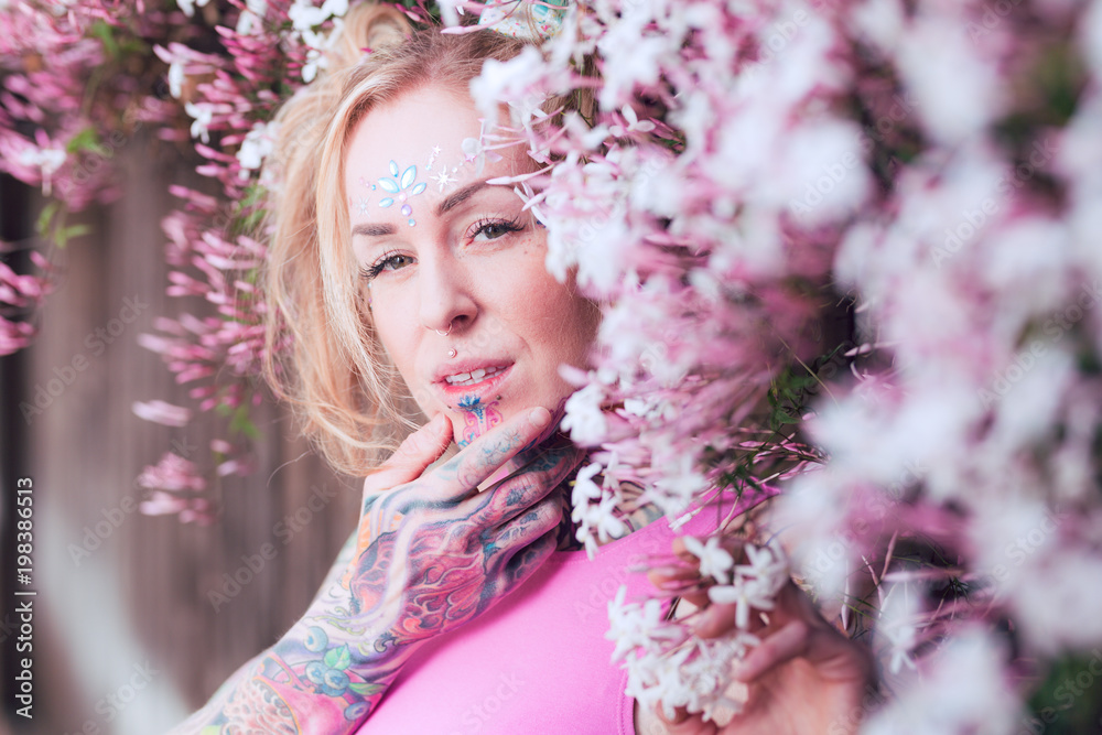 Tight portrait of blonde caucasian woman with tattoos near pink flowers Tight portrait of blonde caucasian woman with tattoos near pink flowers