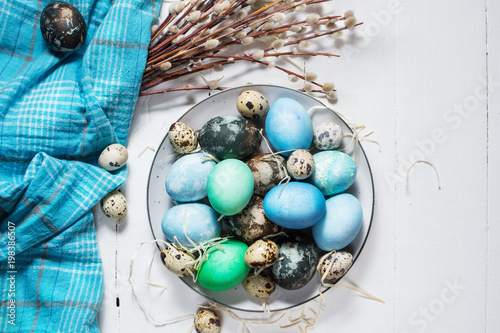 painted eggs on plate, quail and chicken eggs, paint and brush on white wood background, Easter decorations photo