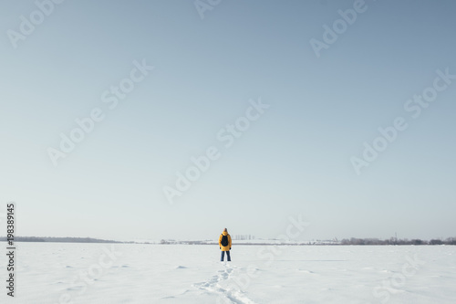 Alone traveler in yellow jacket with black backpack on snowy winter field
