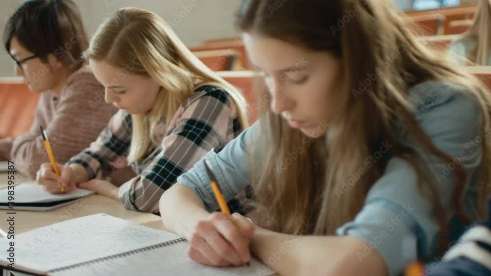 Row of Multi Ethnic Students in the Classroom Taking Exam/ Test/ Writing in Notebooks. Bright Young People Study at the University. Shot on RED EPIC-W 8K Helium Cinema Camera. Row of Multi Ethnic Students in the Classroom Taking Exam/ Test/ Writing in Notebooks. Bright Young People Study at the University. Shot on RED EPIC-W 8K Helium Cinema Camera.