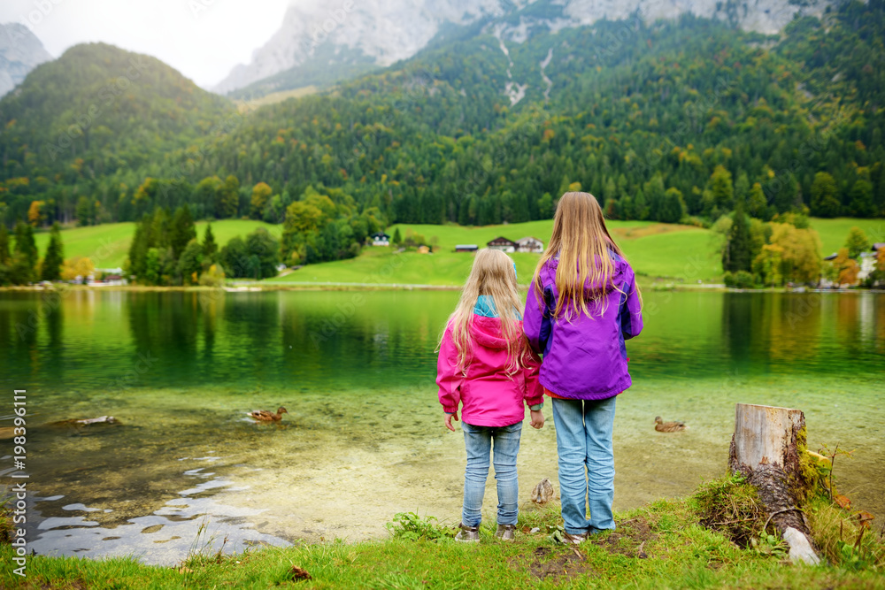 Two little girls enjoying the view of wonderful green waters of Hintersee lake. Amazing autumn landscape of Bavarian Alps on the Austrian border, Germany.