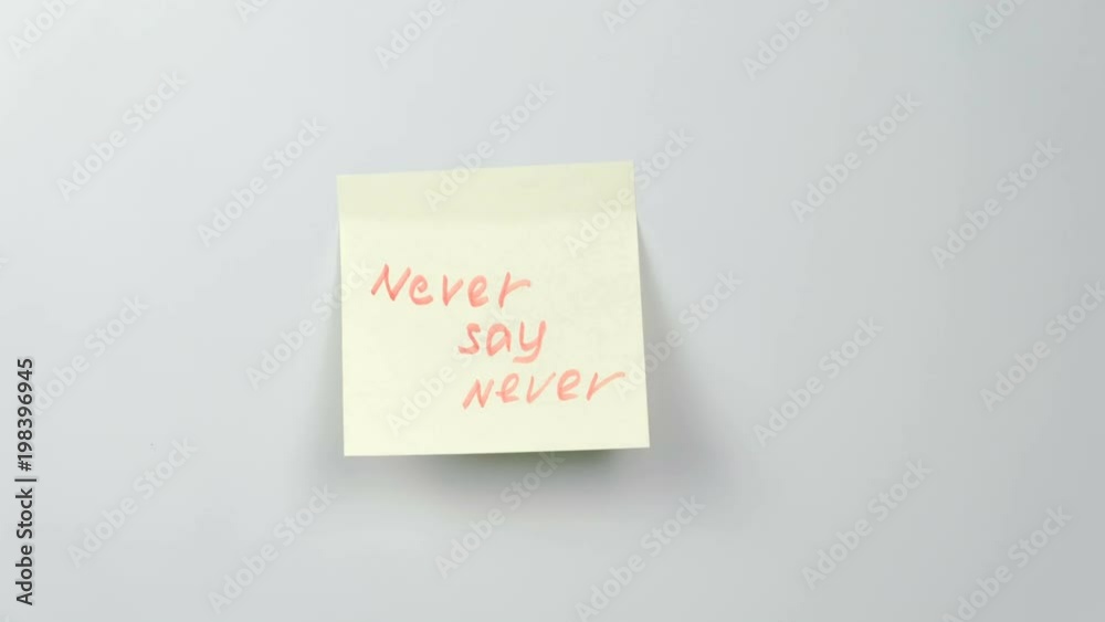 Closeup woman's hands stick yellow sticker paper sheets with words never say never. Closeup woman's hands stick yellow sticker paper sheets with words never say never.
