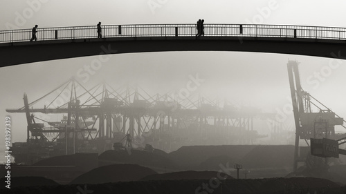 Industriegebiet / Hafen: Kohleverladung, im Vordergrund Fussgängerbrücke mit Personen – sw, Silhouetten