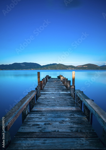 Fototapeta Naklejka Na Ścianę i Meble -  Wooden pier or jetty on a blue lake sunset and sky reflection on water. Versilia Tuscany, Italy