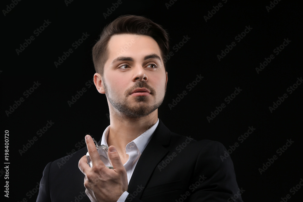 Handsome man in suit using perfume on black background Handsome man in suit using perfume on black background